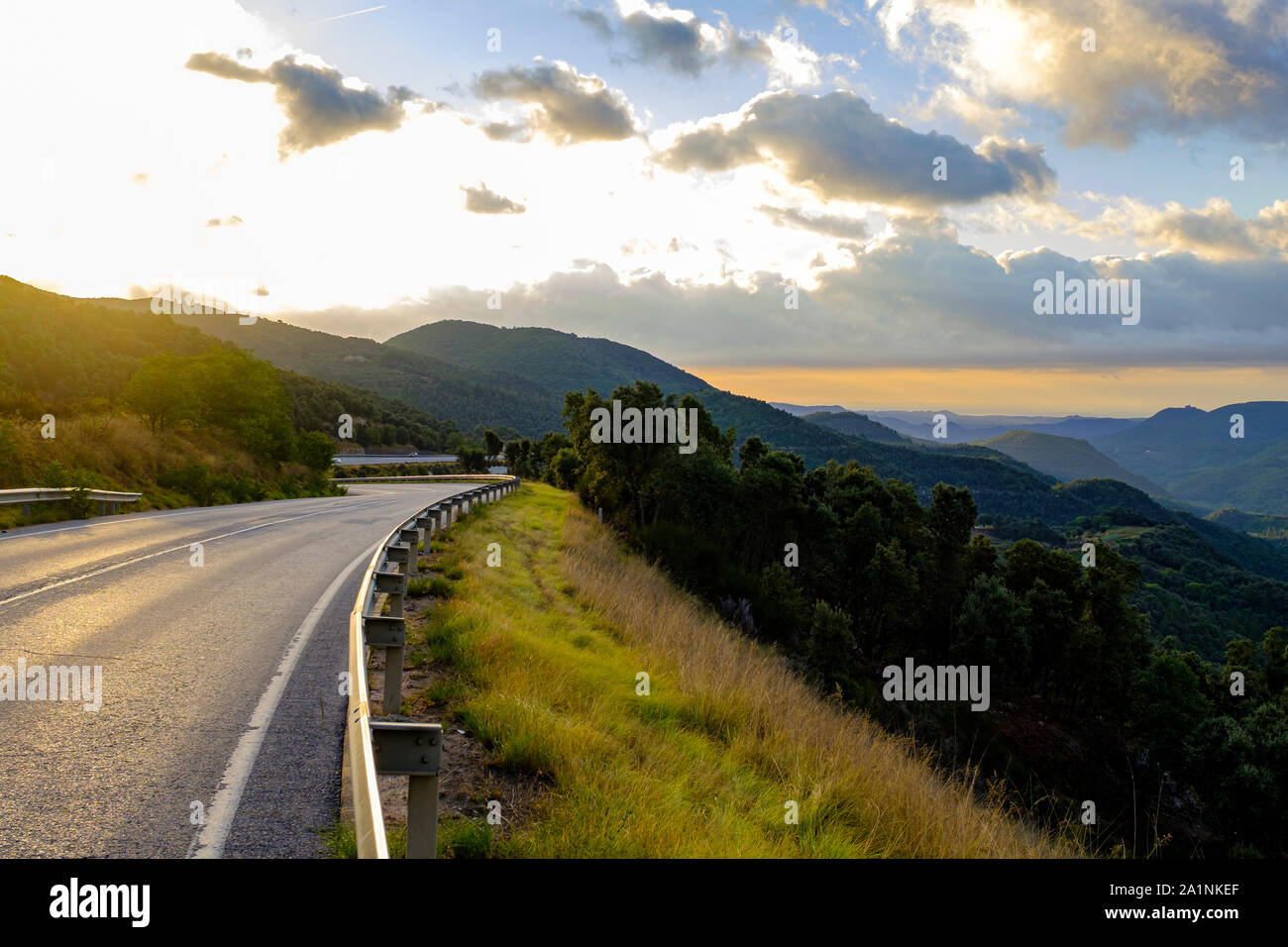 Montagna vuota su strada asfaltata su un verde paesaggio di montagna su un nuvoloso cielo sunrise Foto Stock