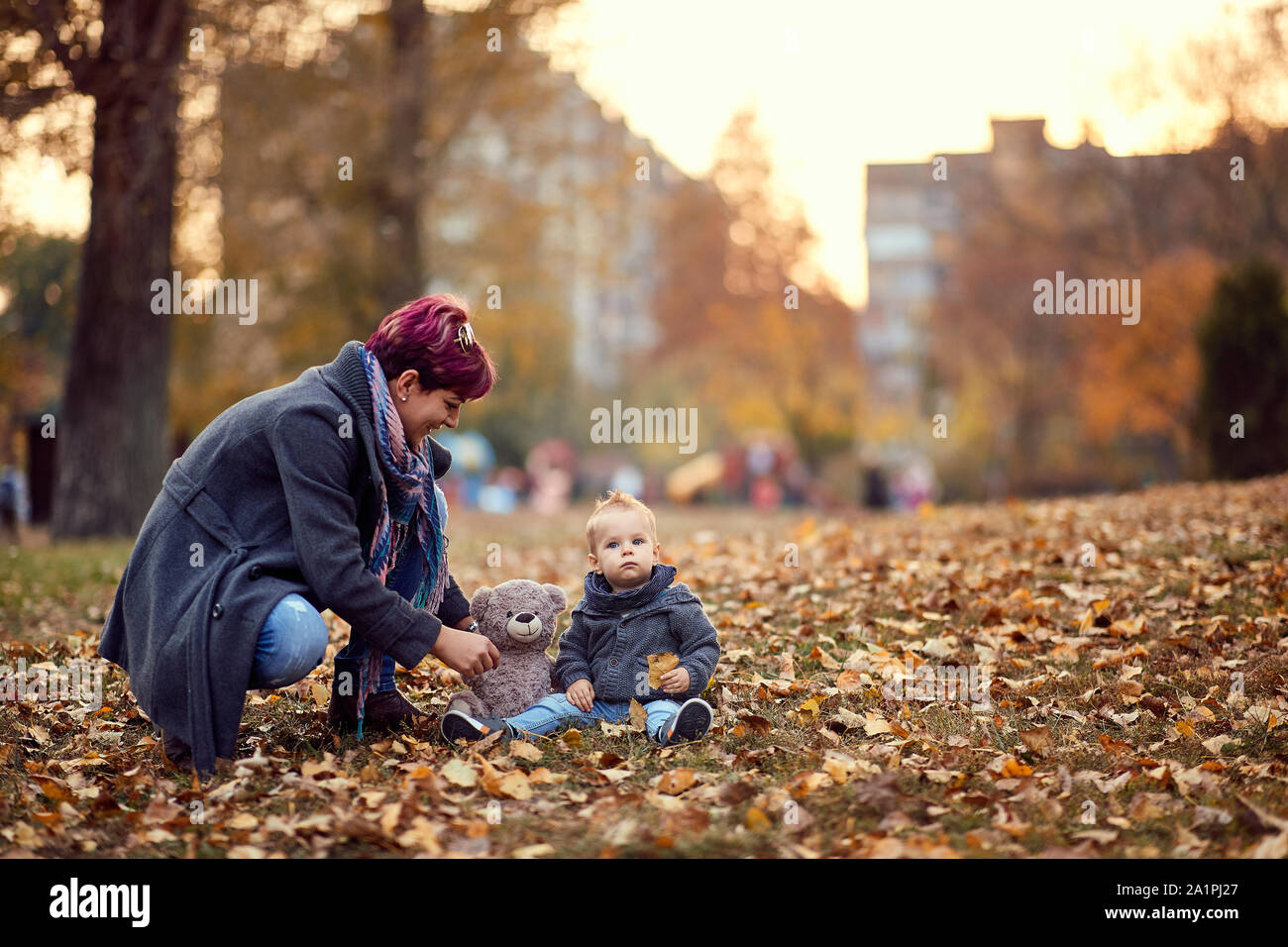 Madre bambino ragazzo giocando, sorridente e divertirsi in autunno il parco della città. Di colore giallo brillante e alberi e foglie Foto Stock