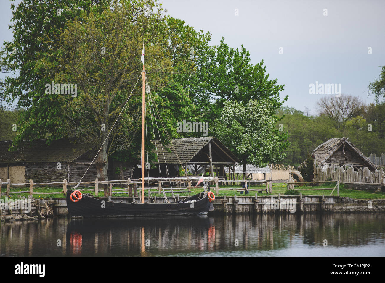 Legno vecchio viking capanne in un villaggio con una nave ormeggiata presso la banca. Foto Stock