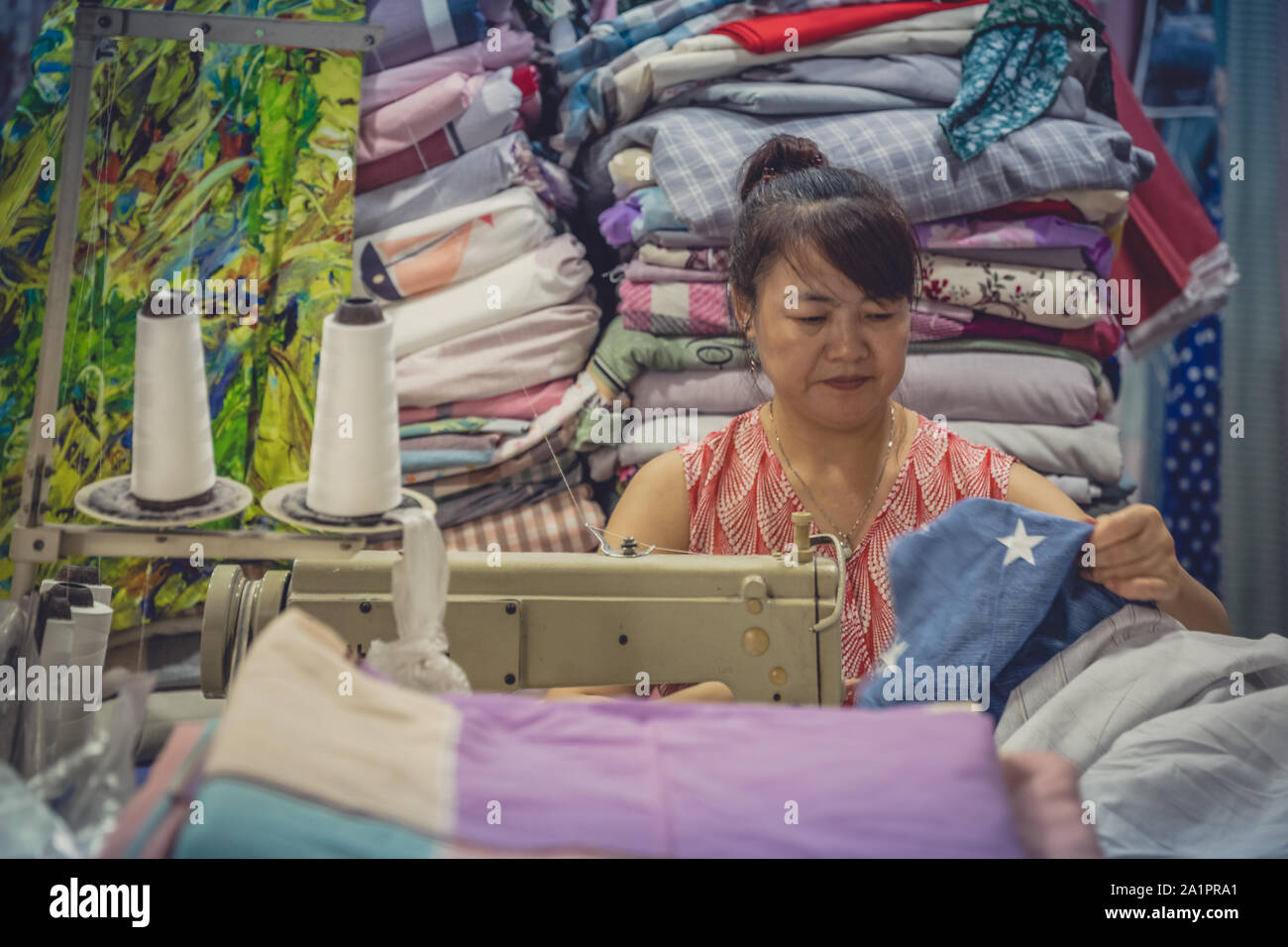 Chengdu, Cina - Luglio 2019 : donna cinese utilizza elettrico macchina da cucire per cucire vestiti nel suo negozio di tessuti Foto Stock