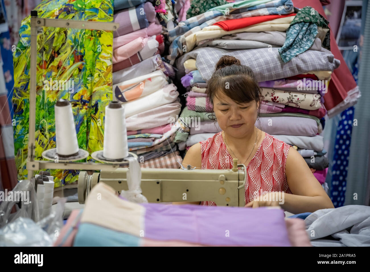 Chengdu, Cina - Luglio 2019 : donna cinese utilizza elettrico macchina da cucire per cucire vestiti nel suo negozio di tessuti Foto Stock