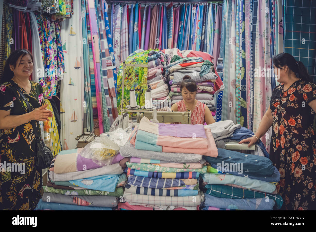 Chengdu, Cina - Luglio 2019 : donna cinese in piedi di fronte ad un piccolo imprenditore tessile e negozio di sartoria Foto Stock