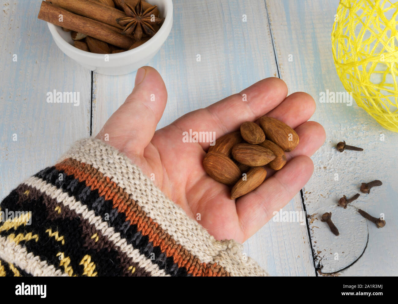 Le mandorle nel palmo della mano in un tradizionale Natale maglione su uno sfondo di colore bianco ciotola con anice stellato e bastoncini di cannella, spruzzò il chiodo di garofano, un Foto Stock