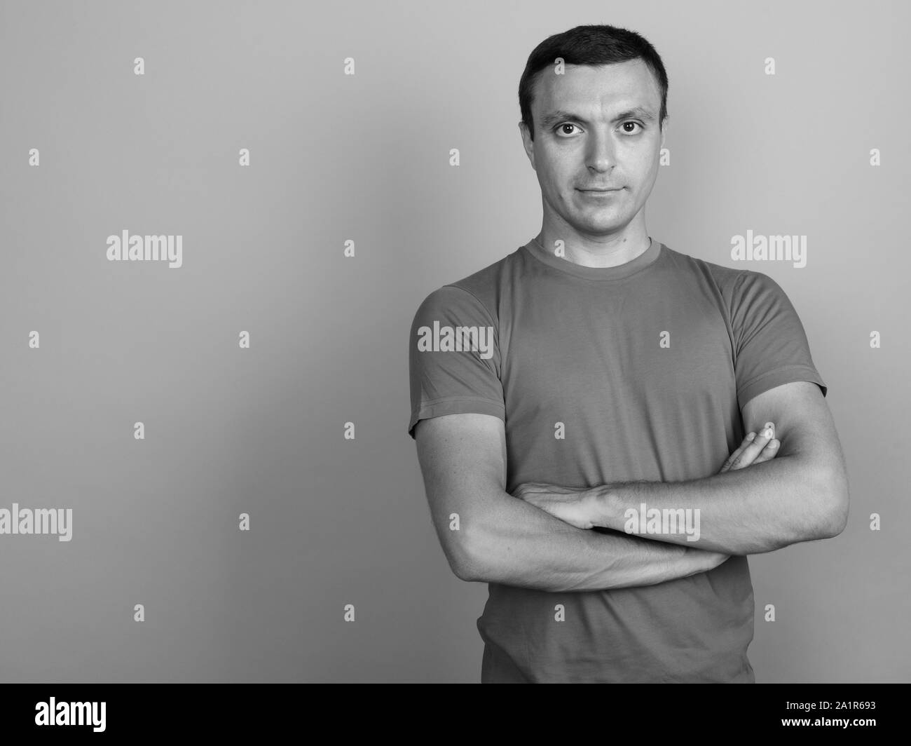 Uomo che indossa la t-shirt contro uno sfondo grigio girato in bianco e nero Foto Stock