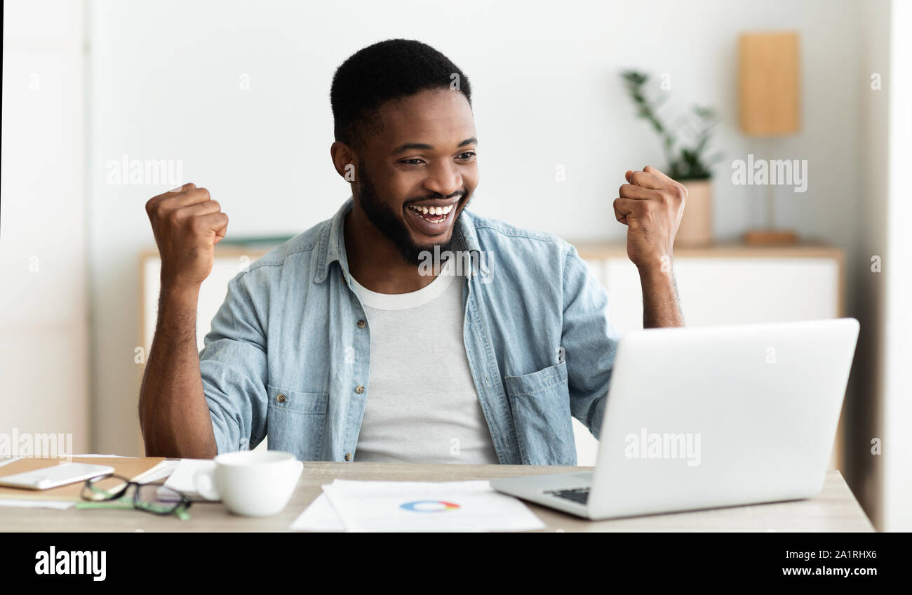 Dipendente nero guardando lo schermo del notebook e celebrare il successo Foto Stock