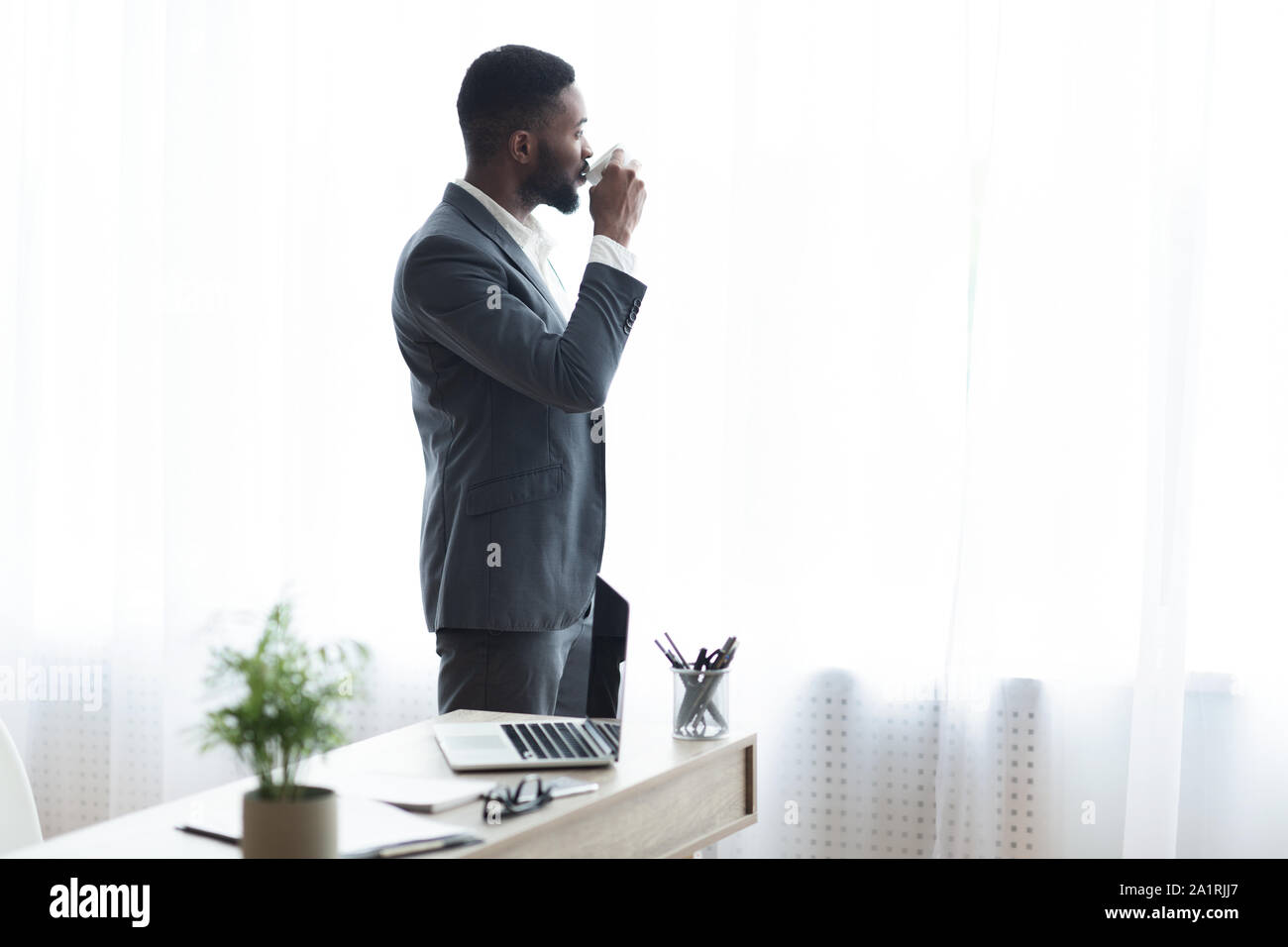 Imprenditore africano a bere caffè e godersi la vista dalla finestra di ufficio Foto Stock