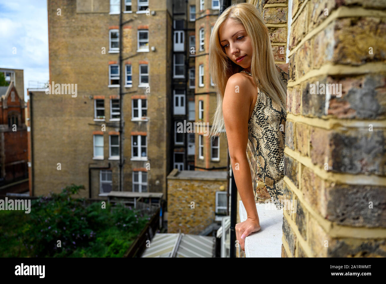 Ritratto di giovane donna con fiducia nei suoi occhi, guardando fuori della finestra di un vecchio edificio in mattoni e sperare per il meglio le cose a venire a Londra Foto Stock