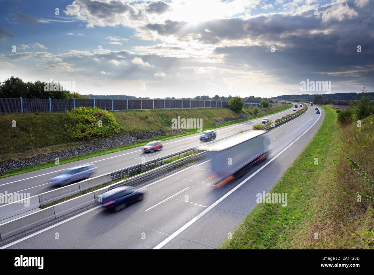 Autostrada nel paese con la guida delle automobili e camion in motion blur sotto un cielo drammatico con le nuvole, concept per il traffico, trasporti e environmen Foto Stock