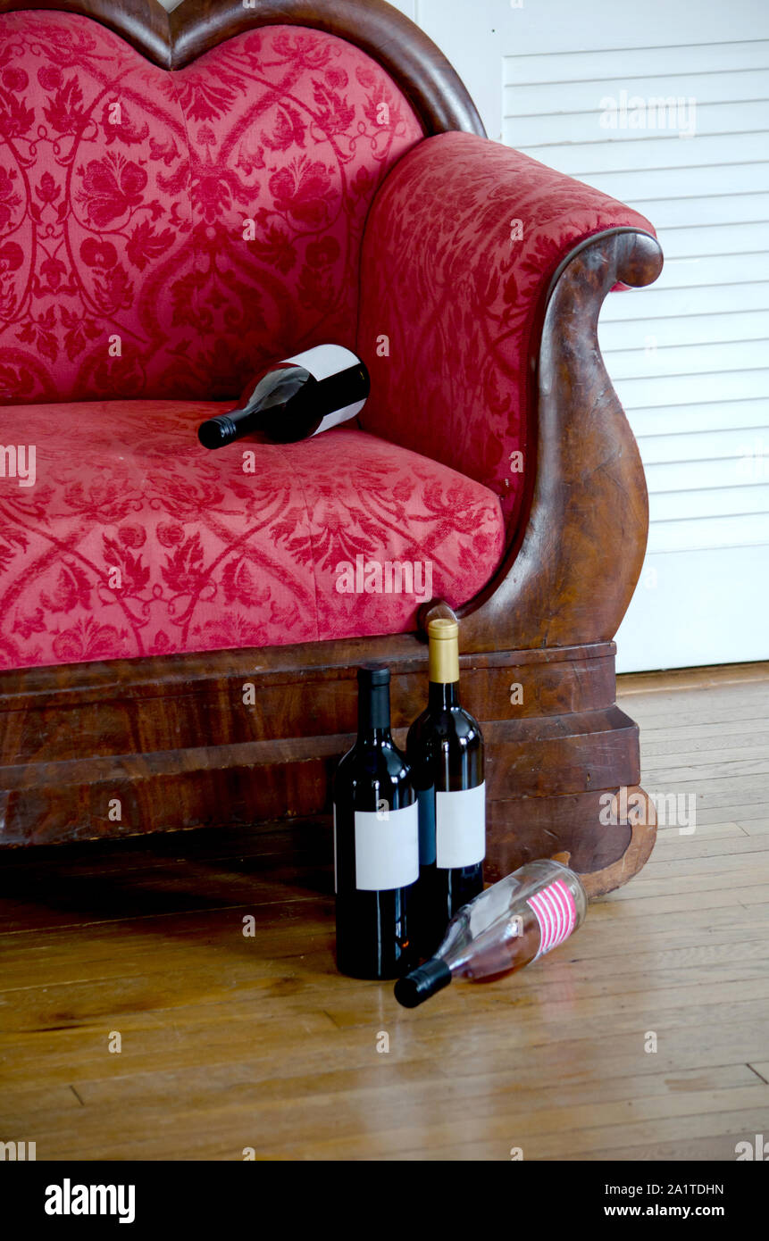 Svuotare le bottiglie di vino si trovano sul pavimento e sulla parte superiore di un'annata divano letto in una stanza vuota. Dove è il partito? Foto Stock