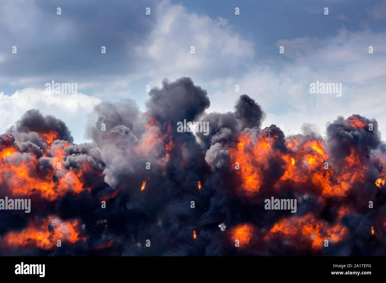 Una gigantesca esplosione crea enormi palle di fuoco e spesso nero fumo, riempimento di un altrimenti pacifica cielo blu Foto Stock