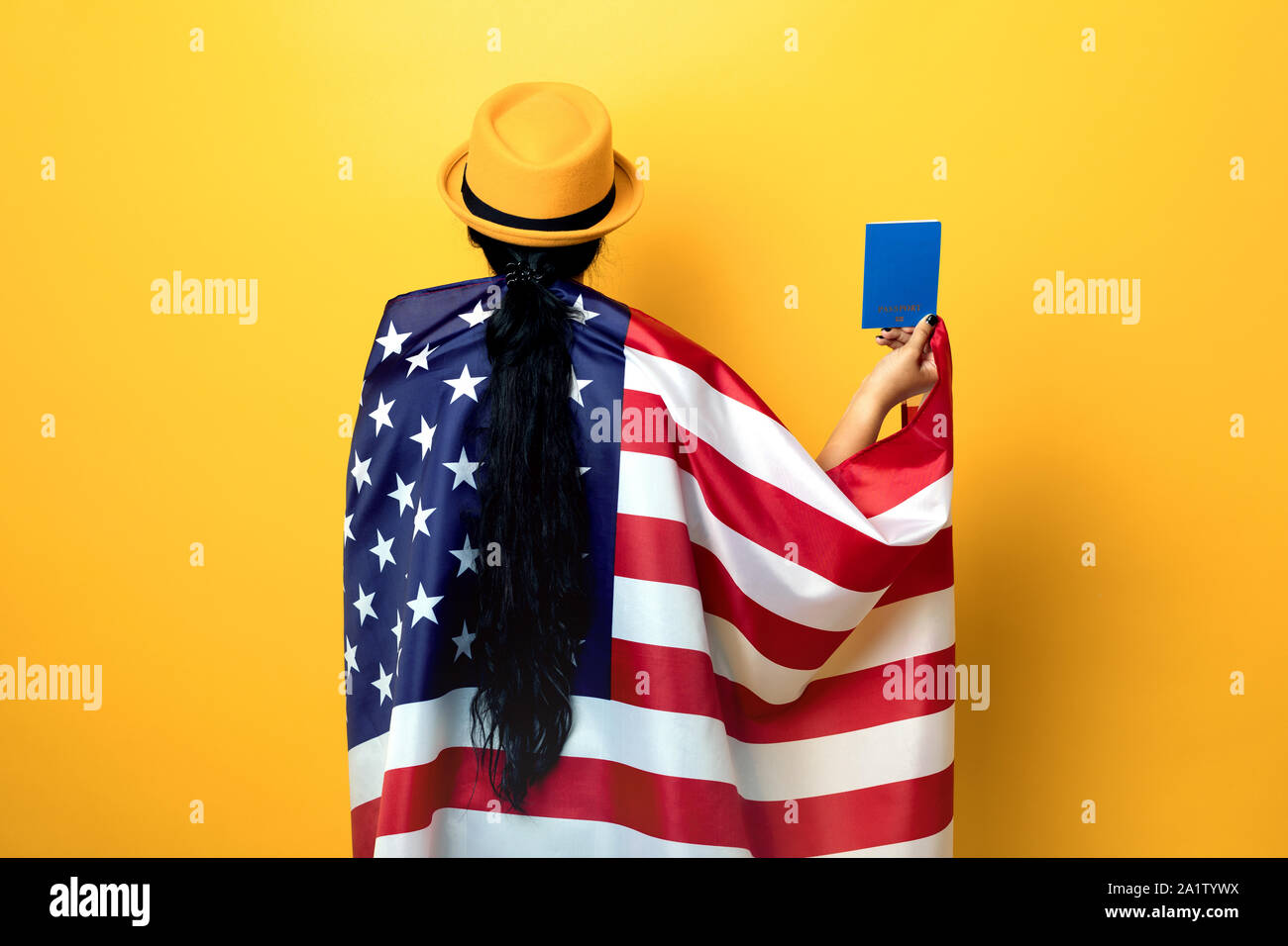 Ragazza sta con la schiena e tiene la bandiera americana su sfondo giallo, ragazza nel quartiere alla moda di hat con bandiera degli Stati Uniti, donna tenendo il passaporto in mano, ho Foto Stock