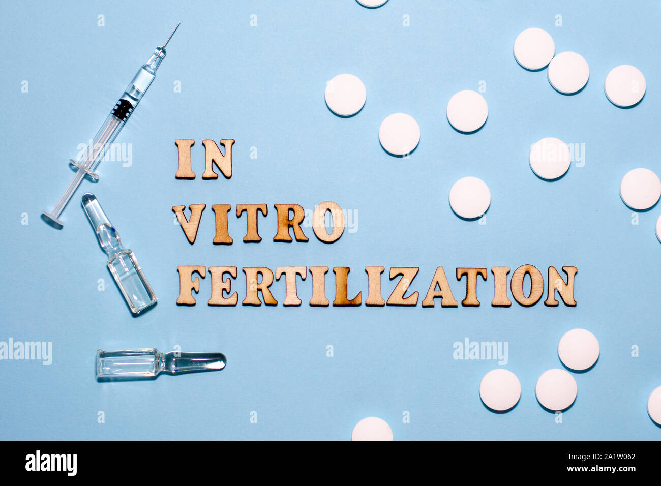 L'iscrizione di fecondazione in vitro è in lettere di legno su uno sfondo blu. In vitro la penna di iniezione, tablet e fiala. Una siringa con un sottile hu Foto Stock
