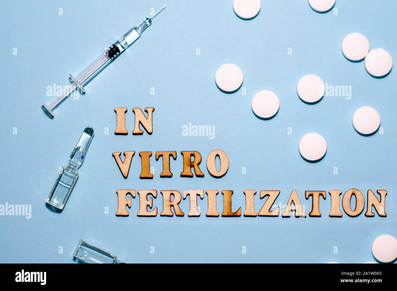 L'iscrizione di fecondazione in vitro è in lettere di legno su uno sfondo blu. In vitro la penna di iniezione, tablet e fiala. Una siringa con un sottile hu Foto Stock