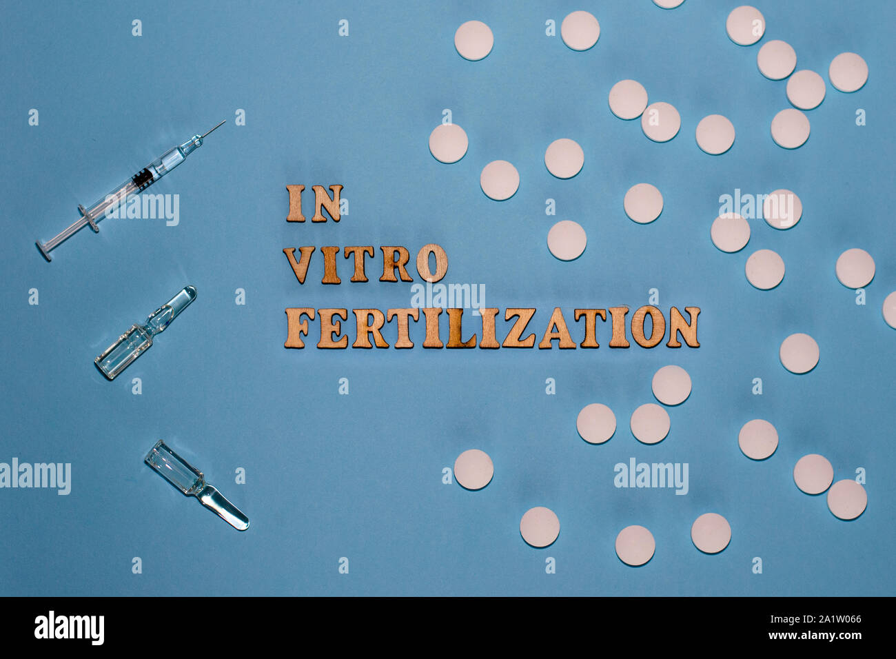 L'iscrizione di fecondazione in vitro è in lettere di legno su uno sfondo blu. In vitro la penna di iniezione, tablet e fiala. Una siringa con un sottile hu Foto Stock