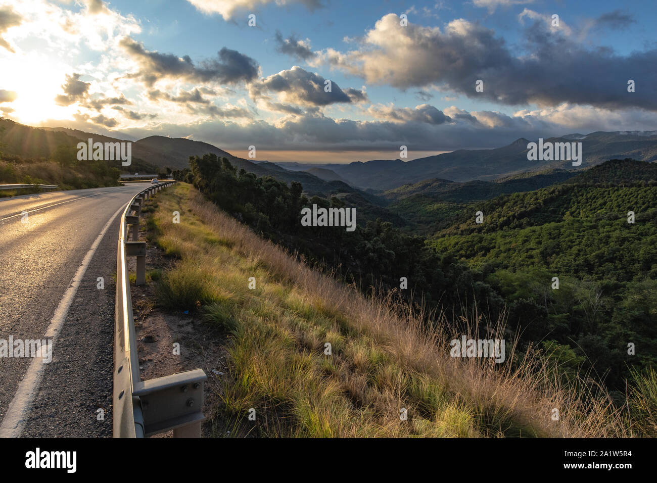 Bordo strada su una montagna traccia vuota in un verde paesaggio di montagna e sole splendente crepuscolo cloudscape Foto Stock