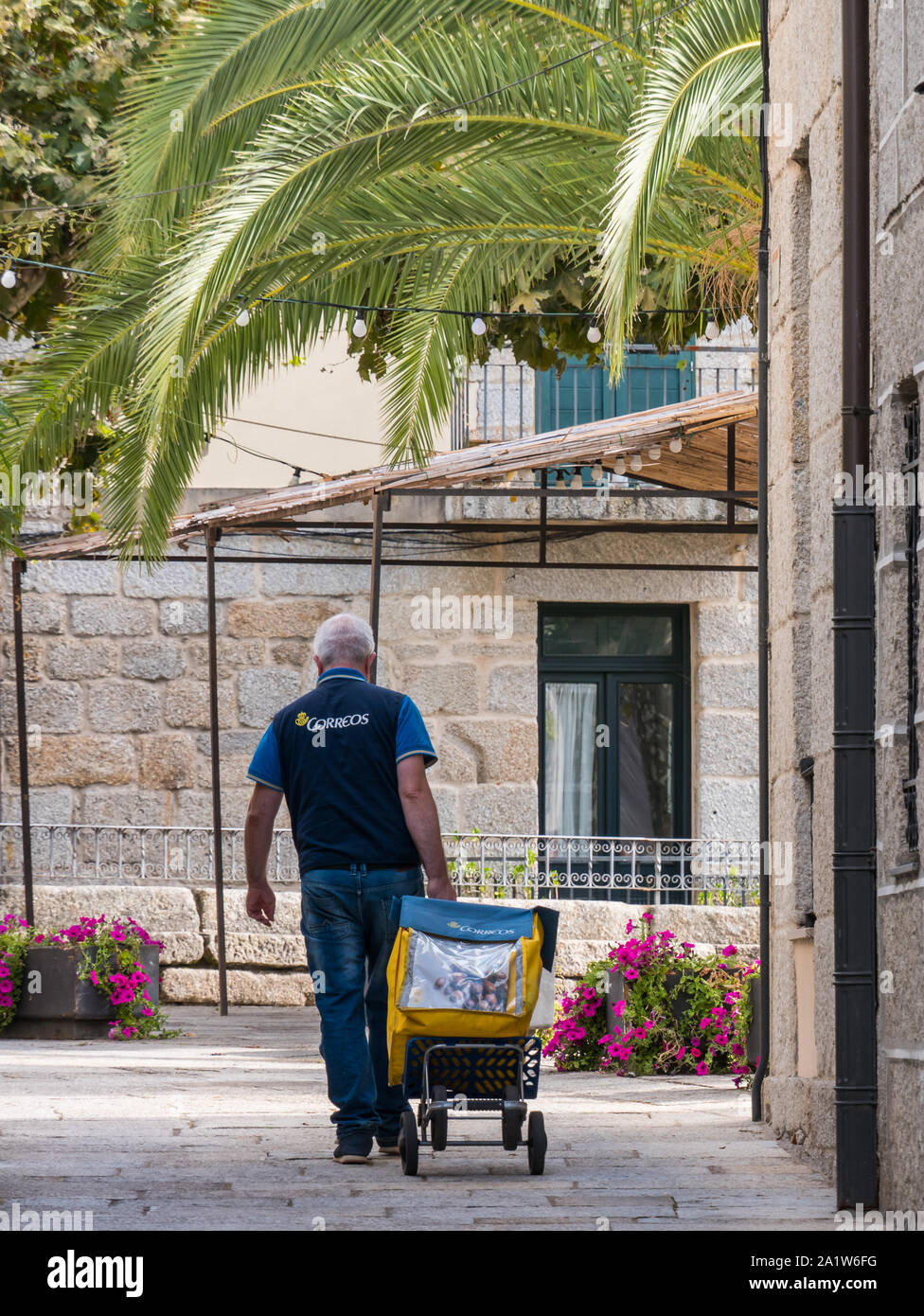 Un postino (spagnolo post company Correos) tirando il suo carrello attraverso le strade della città Foto Stock