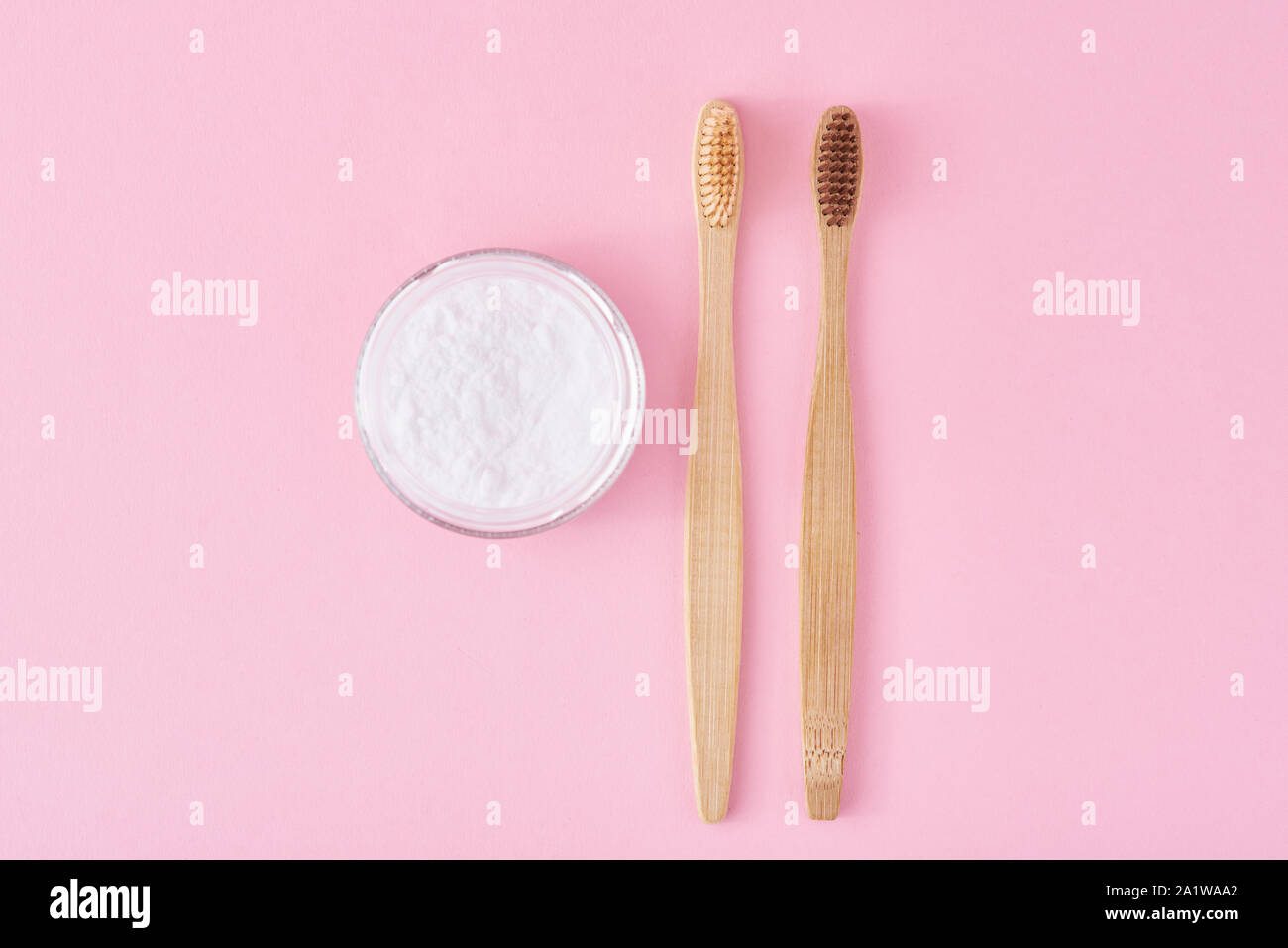 Due di legno spazzolini da denti di bambù e di bicarbonato di sodio in polvere in un barattolo di vetro su sfondo rosa. La salute dei denti e mantenere il concetto di bocca Foto Stock