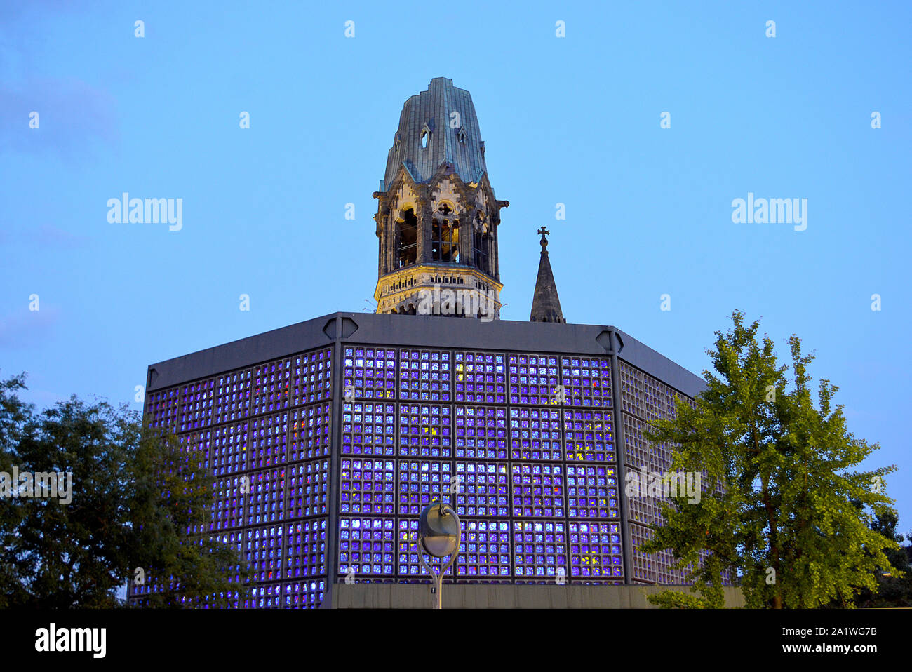 Berlino, Germania - 18 settembre 2019: le finestre in vetro blu della nuova chiesa illuminata di sera con la torre danneggiata a sinistra come un memoriale di guerra Foto Stock