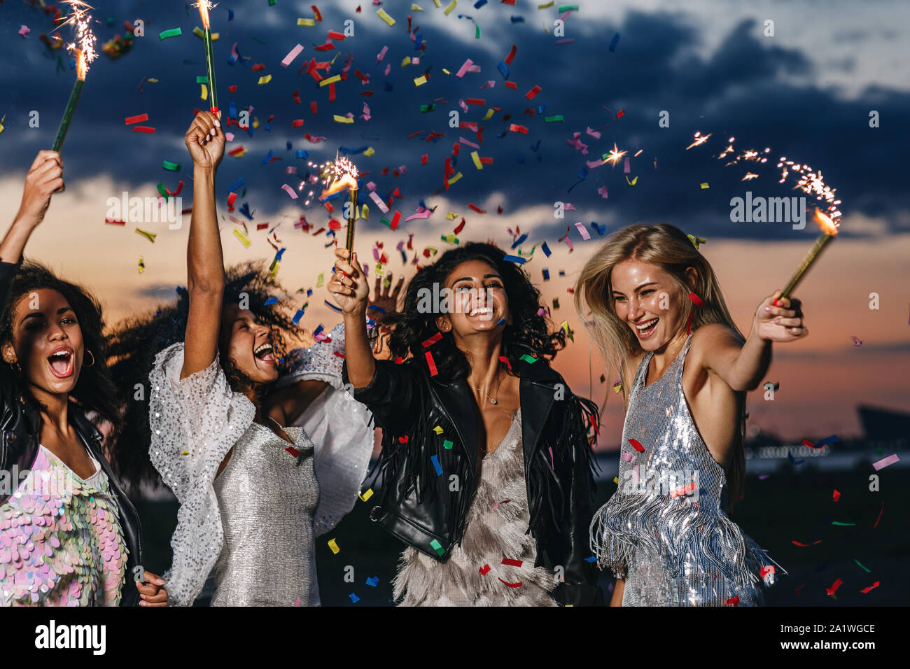 Il gruppo di quattro felici donne ballando con botti sotto i confetti al tramonto Foto Stock