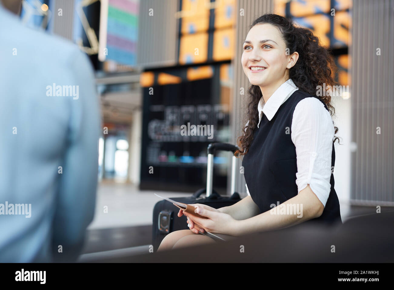 Ritratto di sorridente giovane donna in aeroporto in sala d'attesa godendo di conversazione con un amico, spazio copia Foto Stock