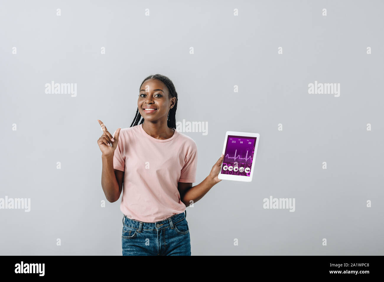 African American donna holding tavoletta digitale con applicazione fitness e puntando con il dito isolato su grigio Foto Stock