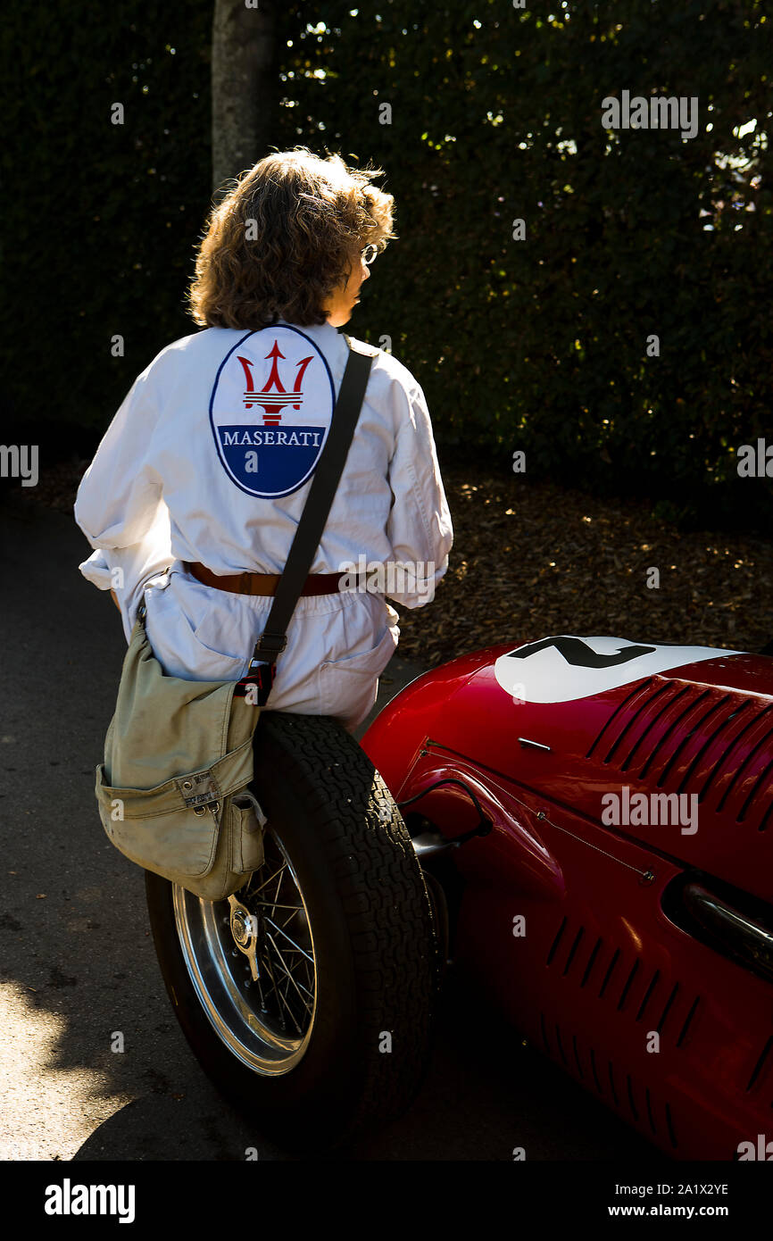 Vista posteriore di lady in tute bianche con logo Maserati seduti sulla ruota anteriore di un rosso vintage racing Maserati auto come disputato il Goodwood Trophy al Foto Stock