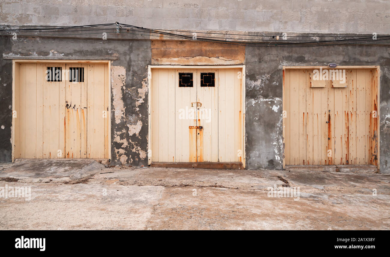 Tre giallo chiuso i cancelli in una fila in una schifezza parete in cemento, porto vecchio facciata di edificio, vista frontale Foto Stock