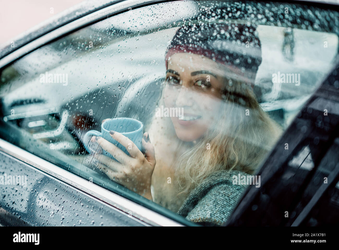 Giovane donna beve caffè e sorridente in auto. Foto Stock