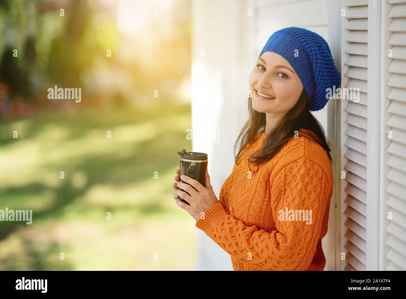Giovane donna con berretto blu beve caffè all'aperto Foto Stock