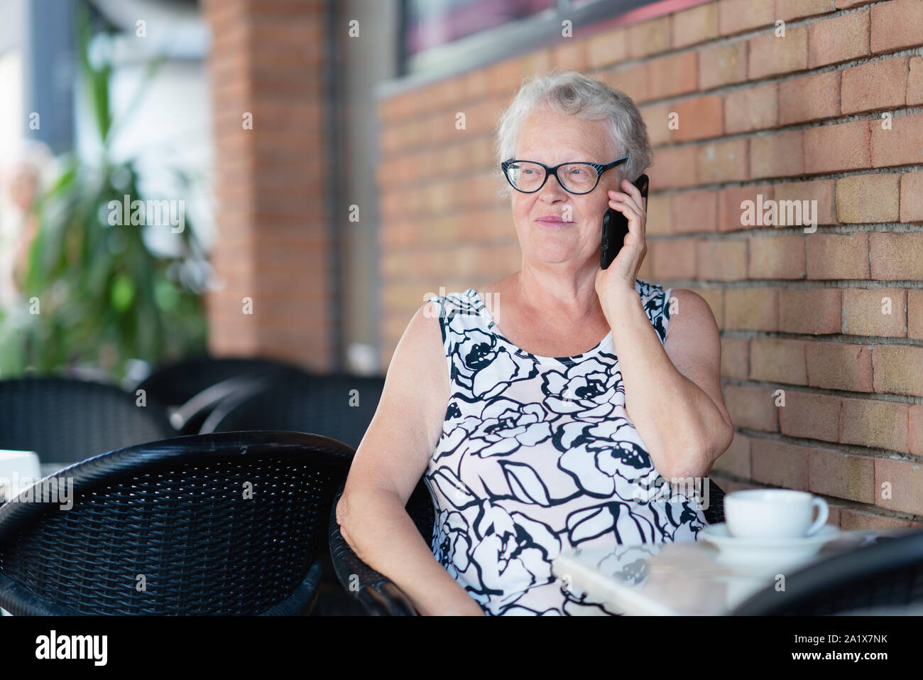 Vecchia donna parla al telefono mentre si beve il caffè Foto Stock