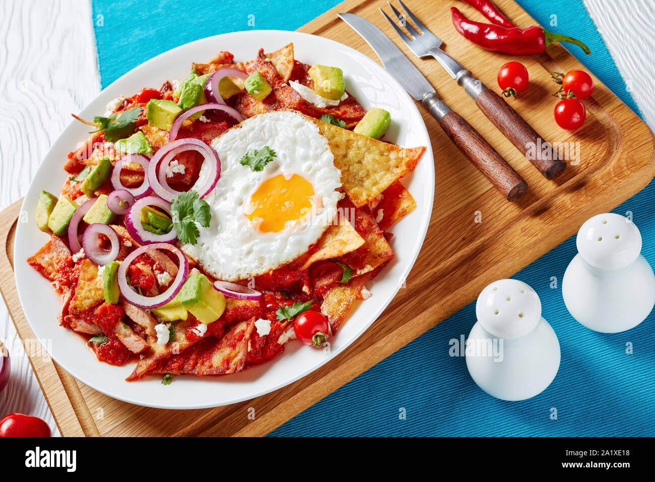 Chilaquiles fatti in casa con un uovo fritto, prosciutto, sbriciolato panela formaggio, avocado e salsa di pomodoro servita su una piastra bianca su un tagliere, piatto messicano, Foto Stock