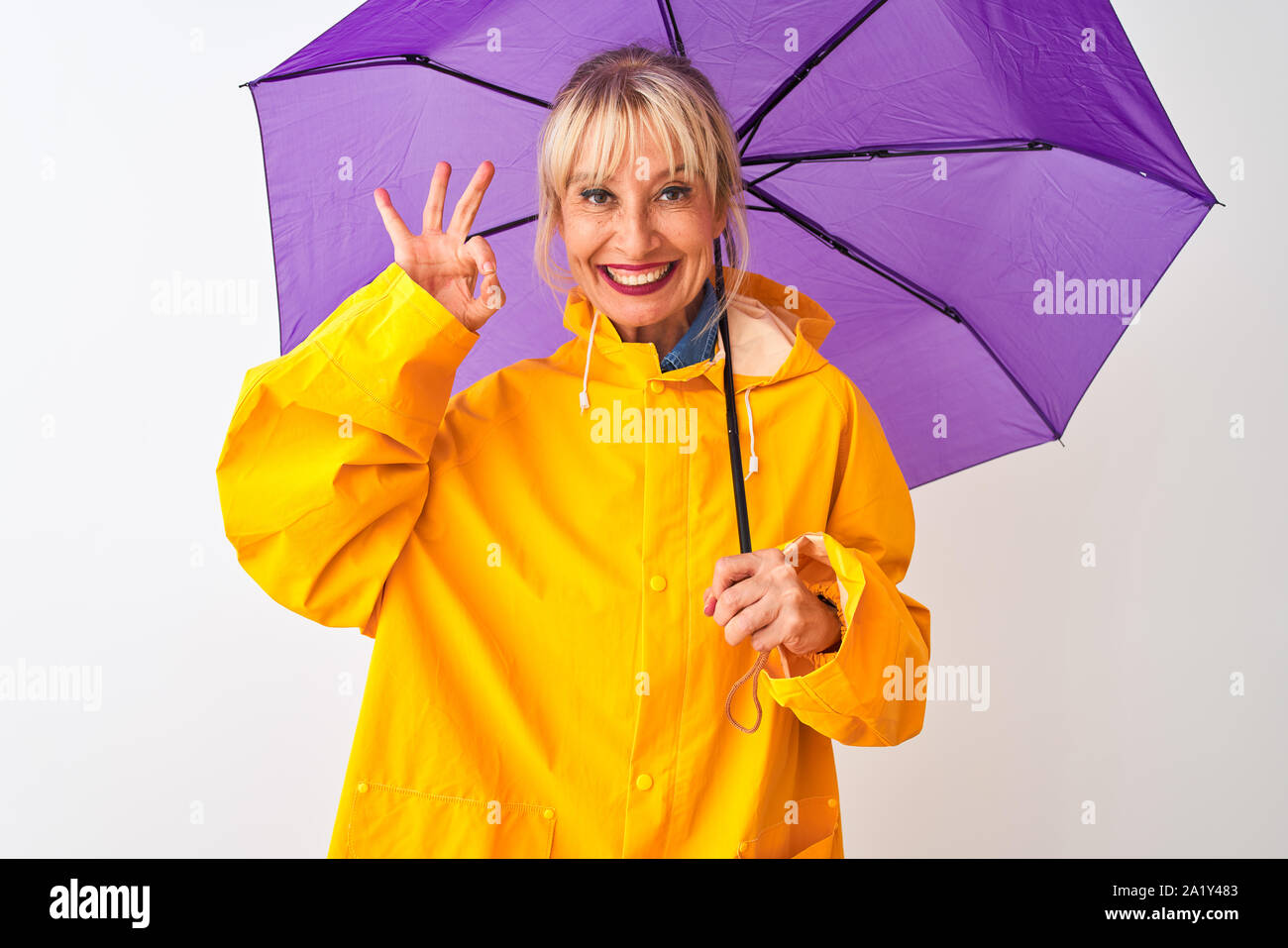 Medioevo donna che indossa la pioggia e il cappotto di viola ombrello isolato su sfondo bianco facendo segno ok con le dita, simbolo eccellente Foto Stock