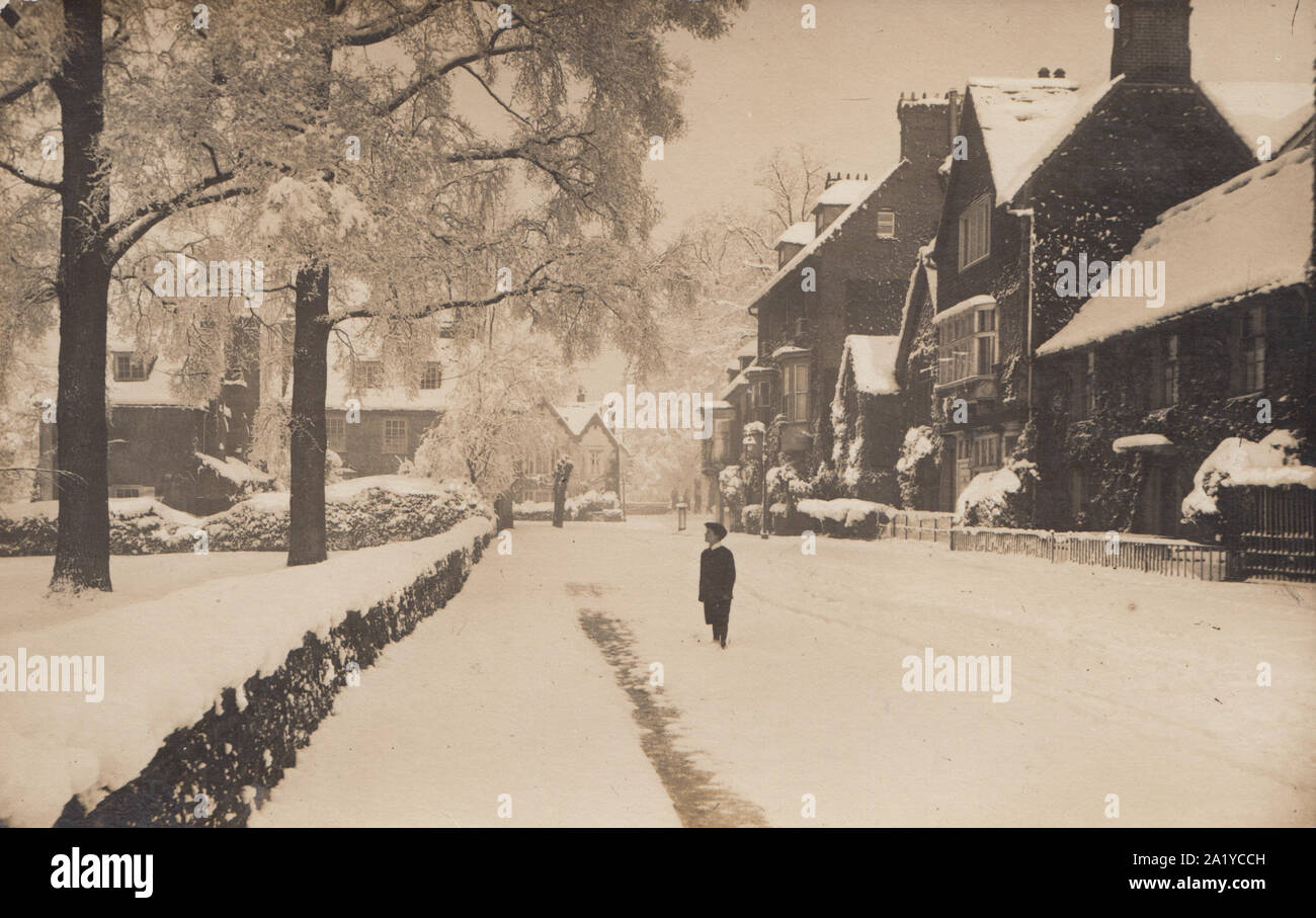 Vintage Edwardian Cartolina fotografica di un British villaggio o città ricoperta di neve. Scolaro si fermò in strada a guardare gli alberi. Foto Stock