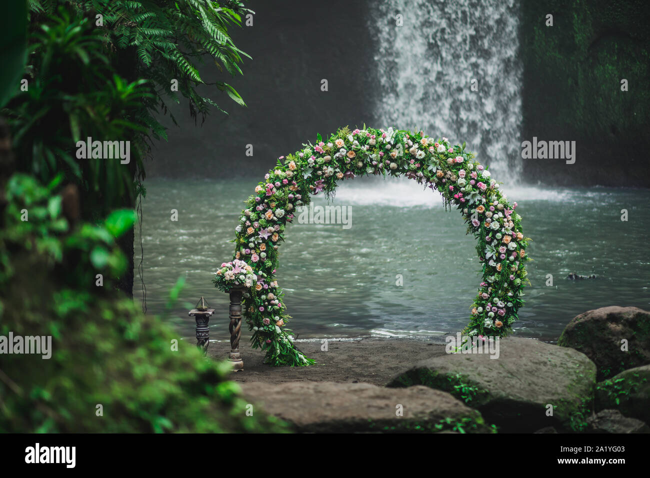 Cerimonia di nozze su Tibumana cascata, Bali. Arco rotondo con fiori freschi nella giungla. Natura insolita concetto di matrimonio. Foto Stock