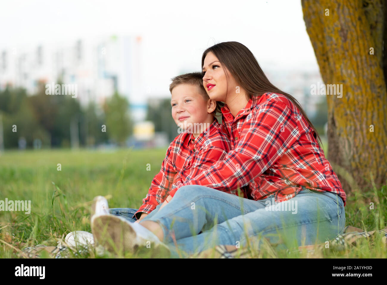 Madre e figlio seduti sul copriletto, abbraccio e guardando in lontananza. Foto Stock