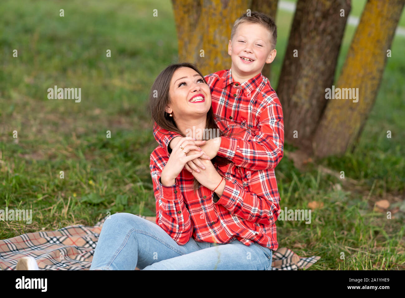 Il Figlio abbraccia delicatamente mom sulle spalle, entrambi felicemente sorridente. Foto Stock