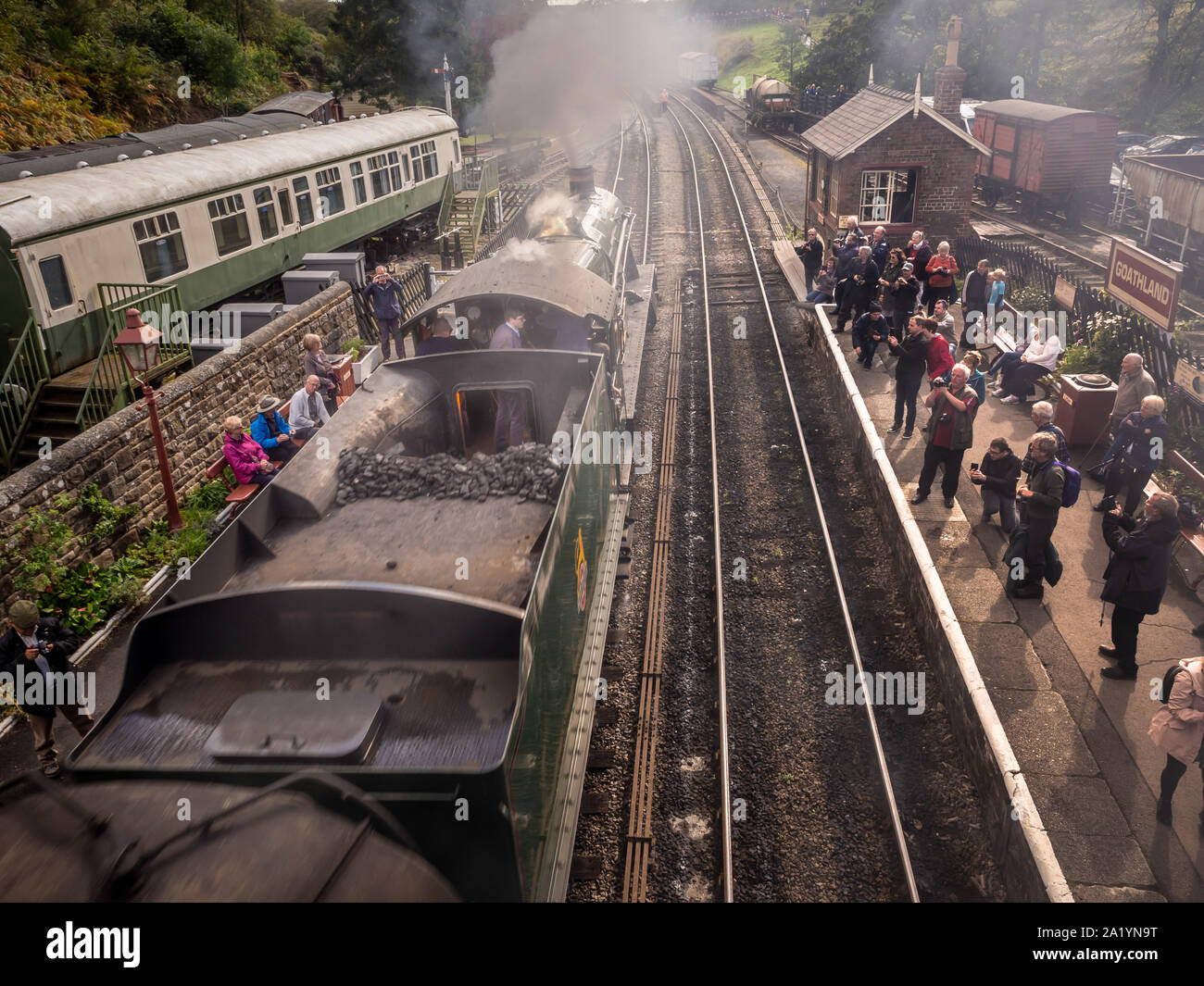 Treno a vapore che arriva alla stazione di Goathland sulla ferrovia North Yorkshire Moors con gli addestratori sulla piattaforma che scattano foto e video Foto Stock