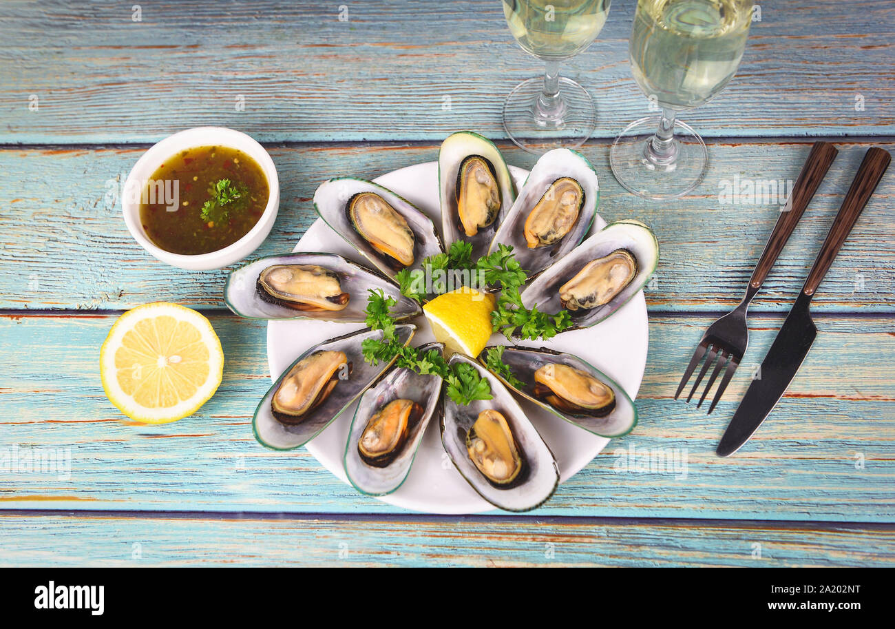 Cozze con erbe aromatiche con limone prezzemolo nella tabella di impostazione / le cozze al vapore e il bicchiere di vino servito sulla piastra bianca salsa di pesce deliziosi pasti su ta Foto Stock