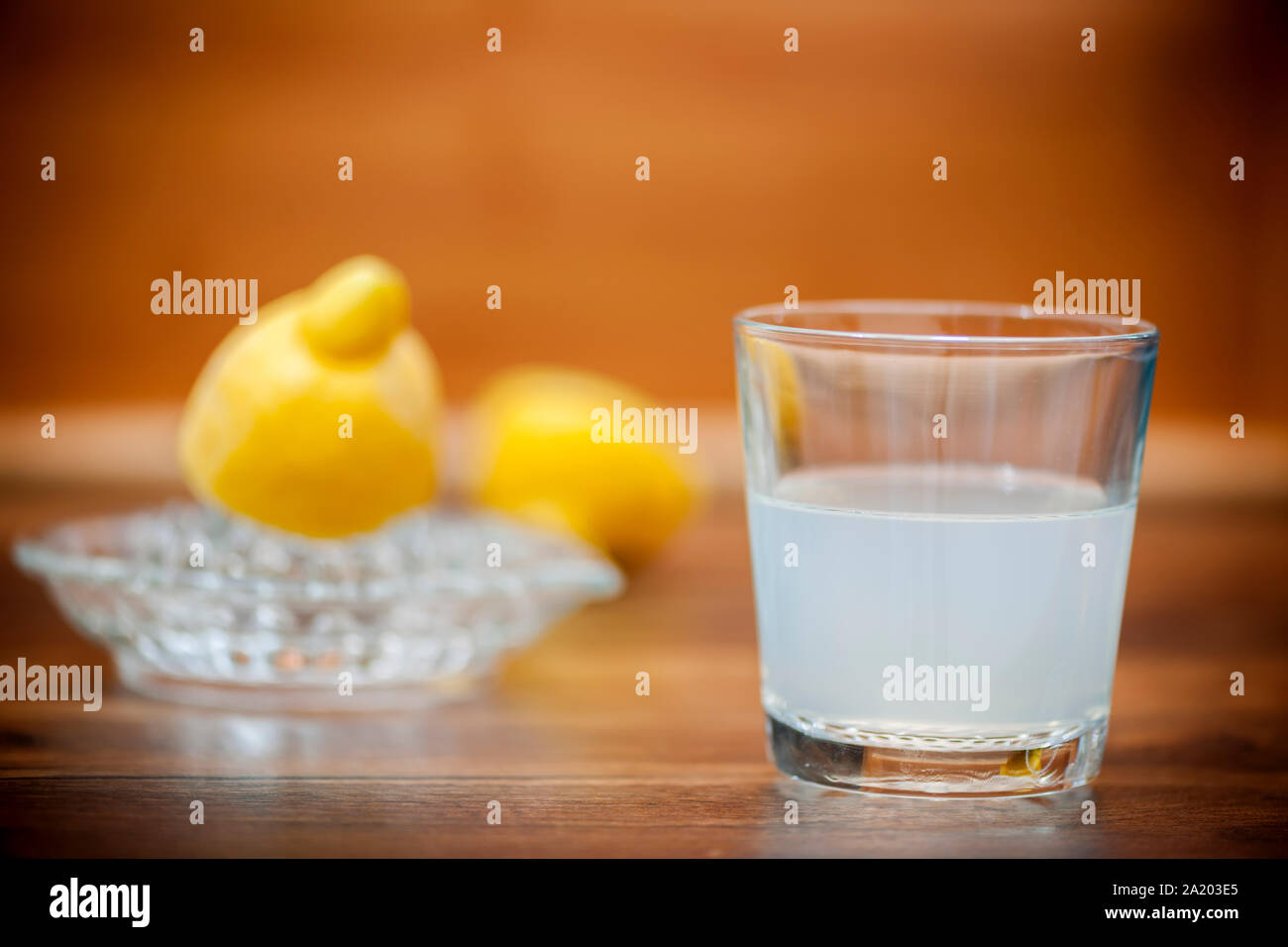 Bicchiere di spremuta di succo di limone su un tavolo da cucina top con dimezzato i limoni e un bicchiere di succo di limone in spremitore il sfondo sfocato. Foto Stock