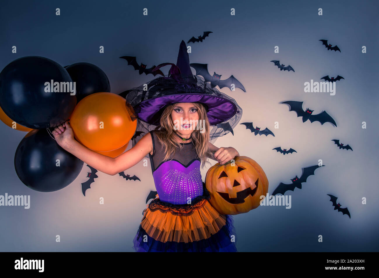 Happy halloween strega & felice di zucca. Bambina con un costume di halloween di una strega con cappello, striped gambe tenendo due smiley zucche di Halloween ja Foto Stock