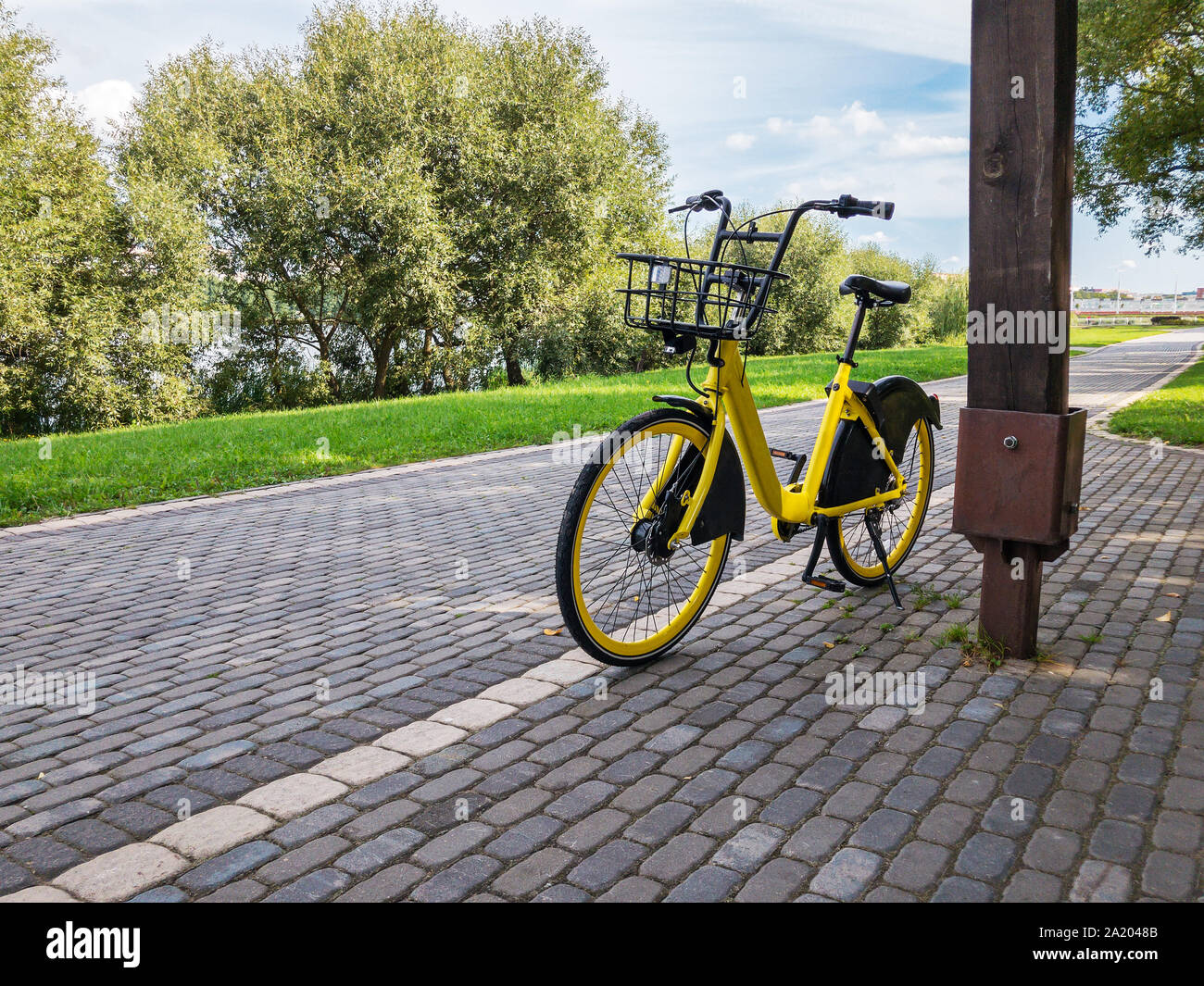 Giallo bicicletta parcheggiata sul viale lastricato in città. Parcheggio Rent-a-servizi bike Foto Stock