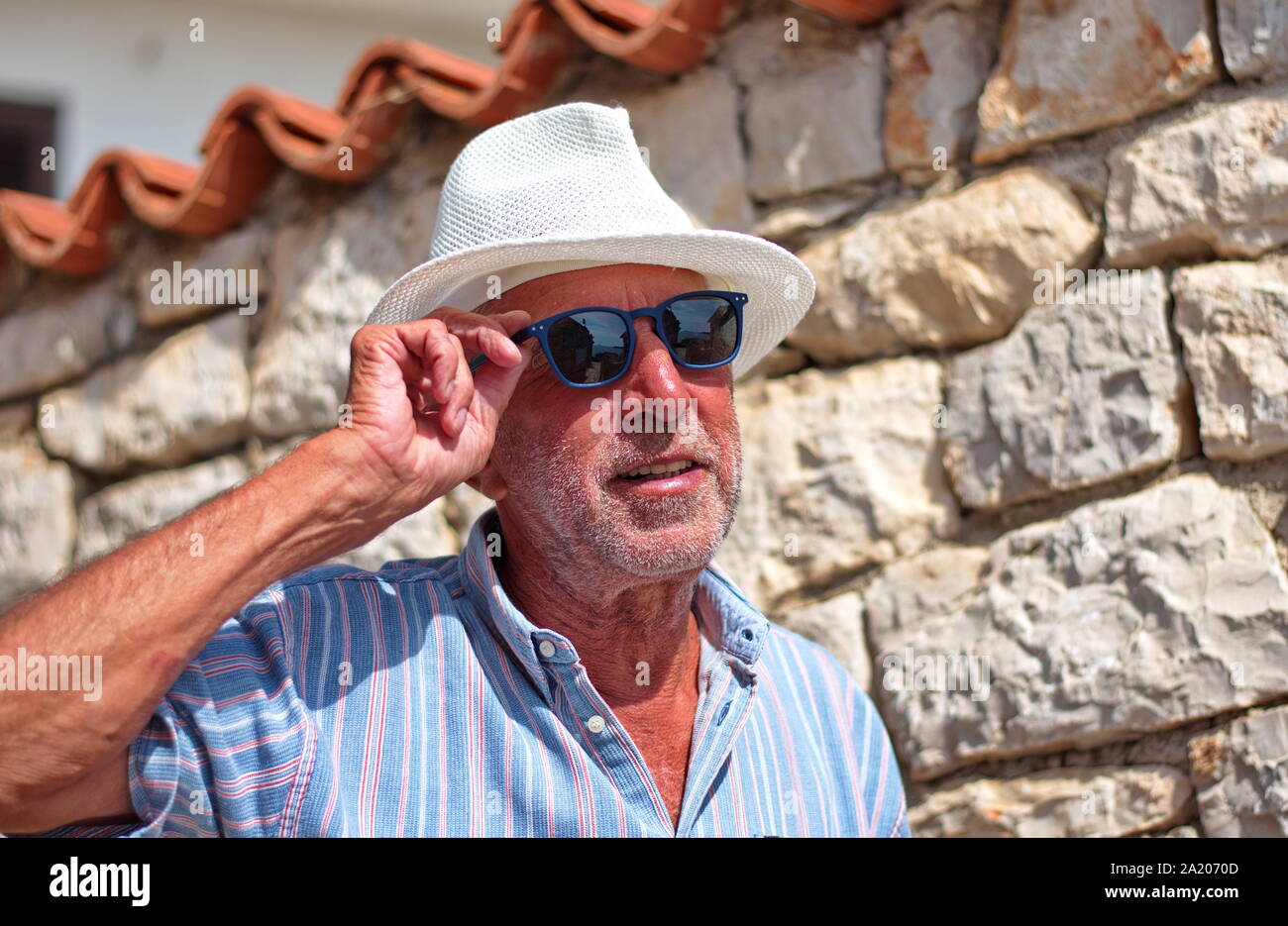 Vita ritratto di un uomo anziano con un cappello contro il muro di pietra Foto Stock