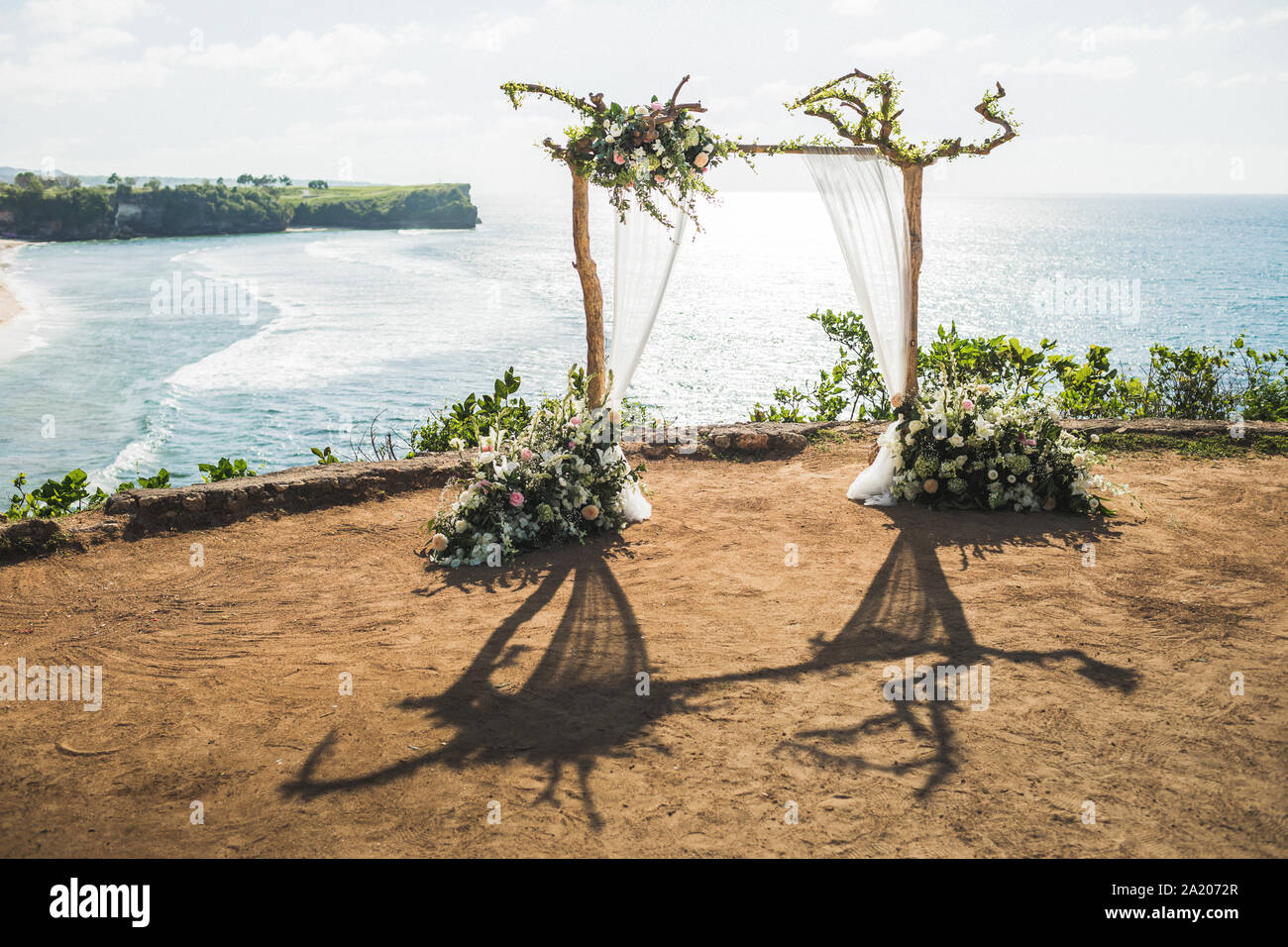 Tramonto cerimonia di nozze arch con rami in legno e decorazioni floreali e panno bianco baldacchino. Vista della scogliera Balangan in Bali. Nozze con vista oceano. Foto Stock