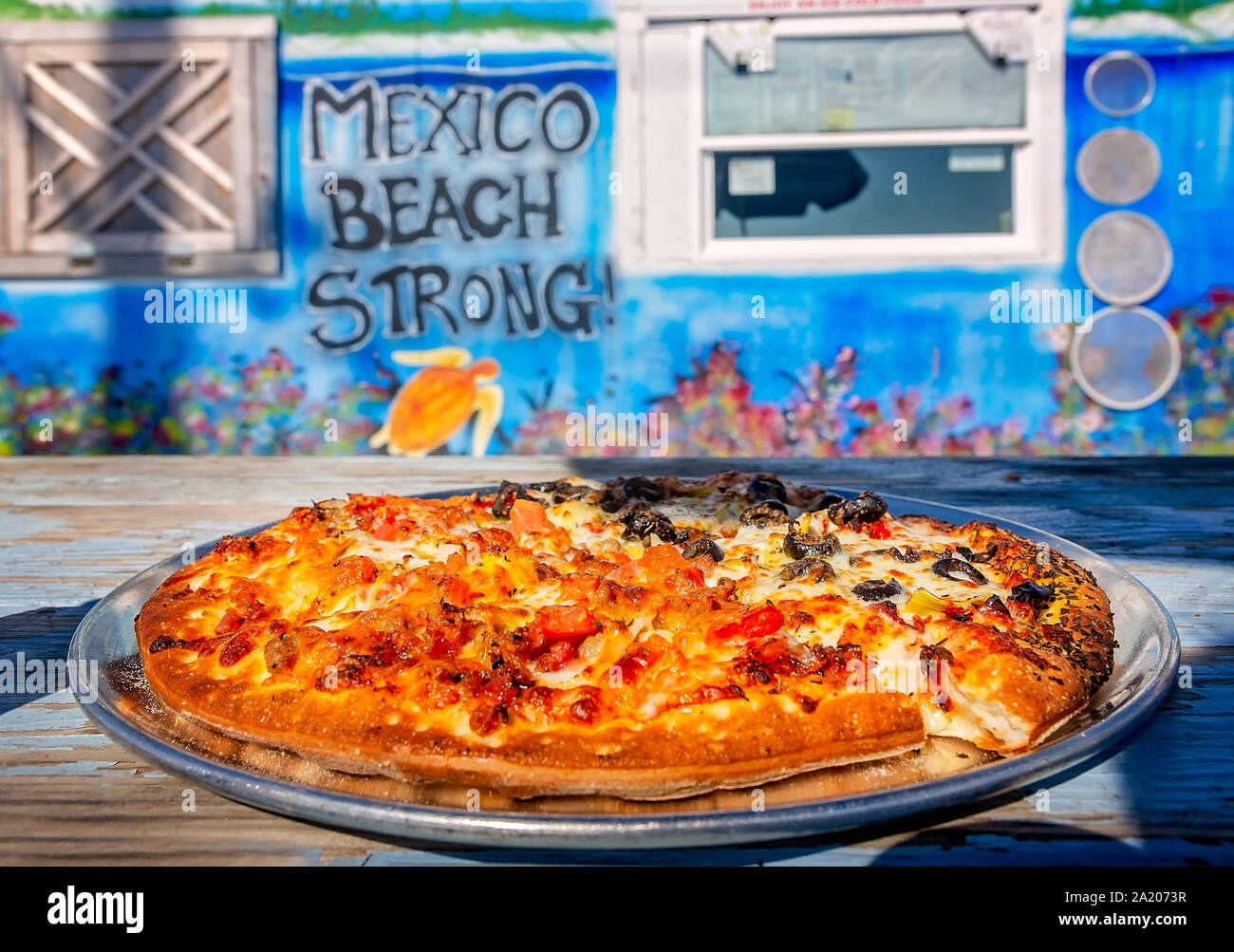 La pizza si siede su un tavolo da picnic nella parte anteriore di una "Messico Beach Strong" murale a Crazy Beach Pizza, Sett. 24, 2019, in Messico Beach, Florida. Foto Stock