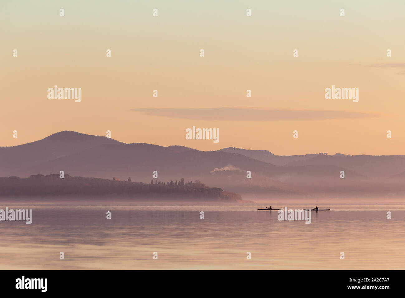 Bellissima vista del lago al tramonto, con toni di colore arancione e due uomini su canoe Foto Stock