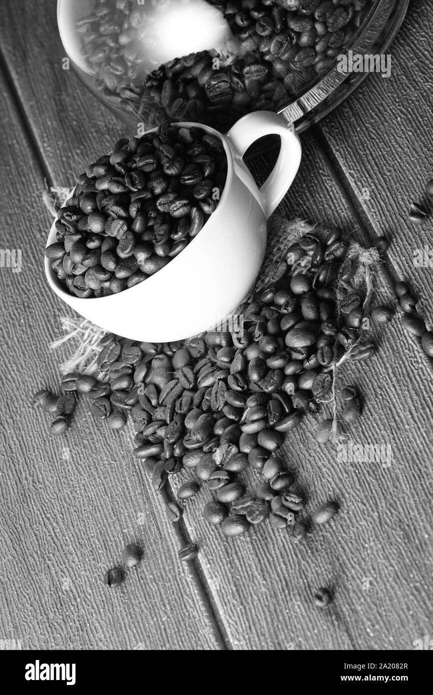 In bianco e nero di chicchi di caffè in una tazza bianca e POT del caffè su una superficie in legno Foto Stock