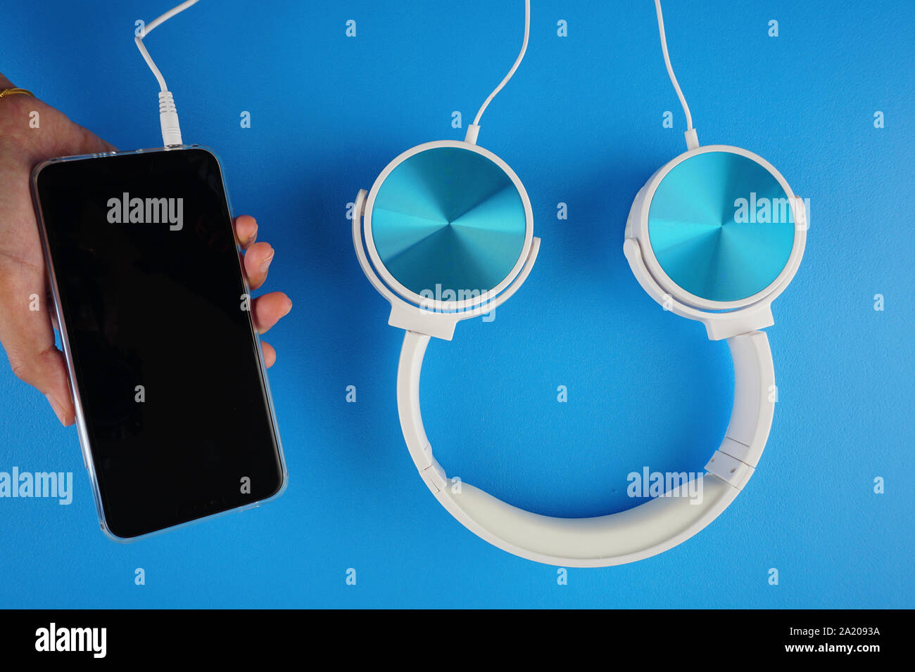 Una mano che tiene un handphone con blu colore bianco cuffie su uno sfondo blu Foto Stock