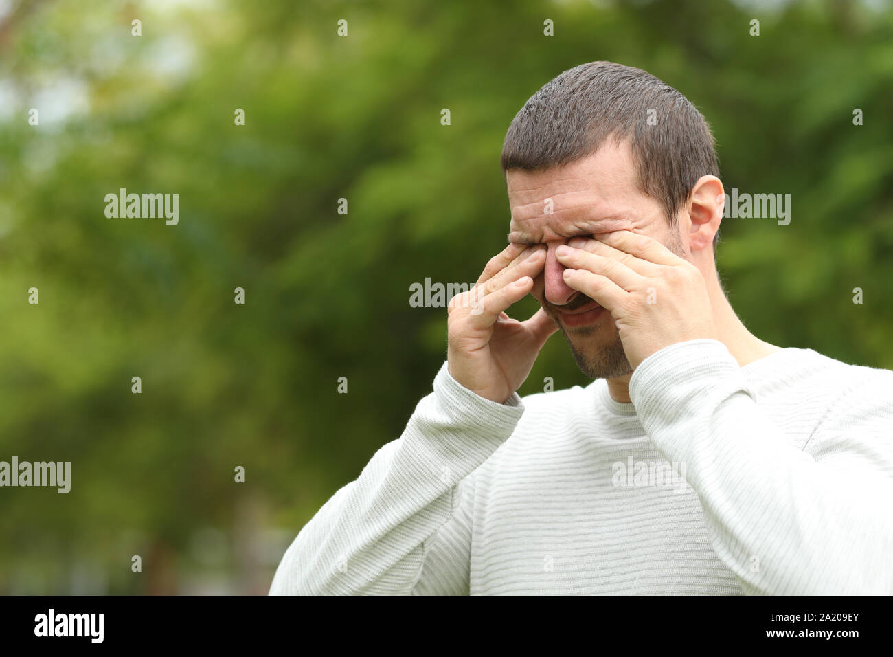 Uomo che soffre di prurito di graffiare gli occhi in piedi da solo in un parco Foto Stock