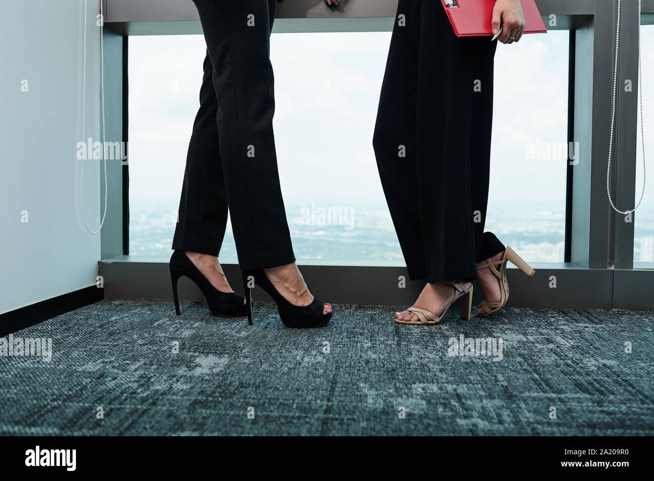 Gambe di imprenditrici in tacchi alti in piedi alla grande finestra in un ufficio moderno e discutere di progetto Foto Stock