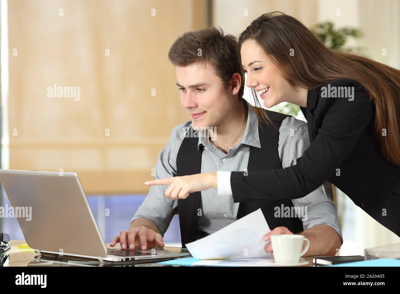 Felice imprenditrice che mostra il contenuto del laptop al suo collega in ufficio Foto Stock